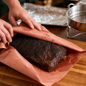 Smoked brisket with dark peppery bark being wrapped in butcher paper