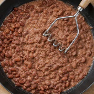 Red beans being mashed with liquid in a skillet