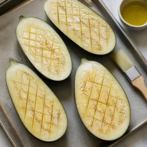 Scored eggplant halves brushed with oil before roasting