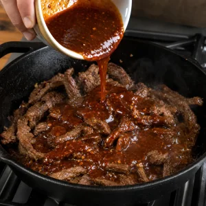 Gochujang soy glaze poured over browned beef strips in a skillet