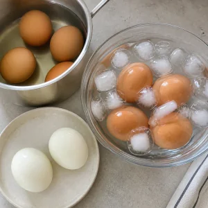 Boiled eggs cooling in ice water beside peeled eggs
