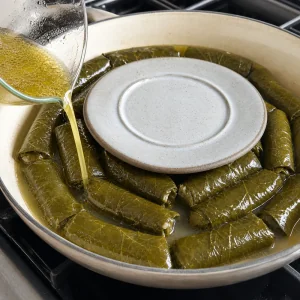 Brühe und Olivenöl werden über Dolmades gegossen, ein kleiner Teller hält sie untergetaucht