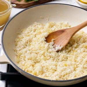 Abgetropfter Reis wird mit Zwiebel und Knoblauch angeröstet, bis er vor dem Köcheln glänzt