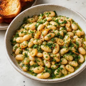 Finished marinated white beans with garlic and fresh herbs in a shallow bowl