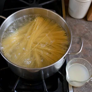 Spaghetti boiling with reserved pasta water nearby