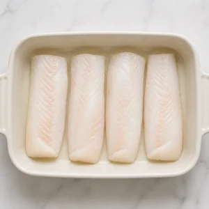 Raw haddock fillets arranged in a buttered baking dish