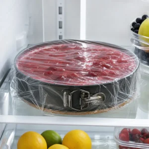 Covered no-bake cheesecake chilling in the refrigerator with red topping visible