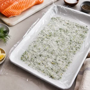Dill salt cure spread on plastic wrap in a tray for the salmon
