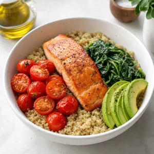 Tigela de quinoa montada com espinafre tomate cereja abacate e salmao selado