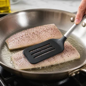 Barramundi fillets pressed skin-side down in a hot skillet with a flexible spatula.