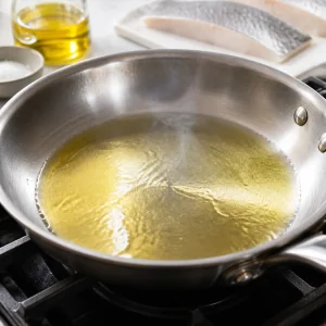 Olive oil shimmering in a hot stainless steel skillet before the fish is added.