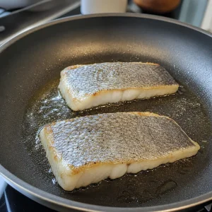 Filetti di barramundi rosolati con la pelle verso il basso in olio d'oliva