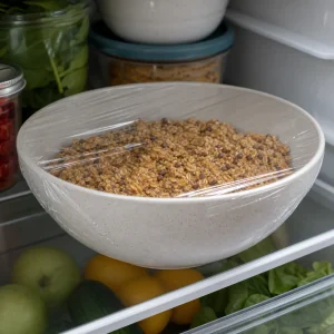 Covered bowl of oat bite mixture chilling on a refrigerator shelf