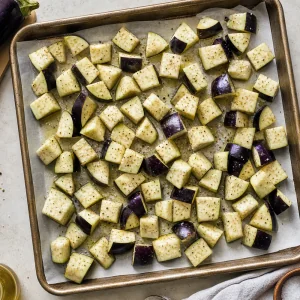 Raw eggplant cubes seasoned with olive oil, salt, and pepper on a baking sheet