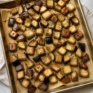 Roasted eggplant cubes browned on parchment in a baking sheet