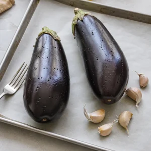 Melanzane intere bucherellate con una forchetta accanto ad aglio non sbucciato