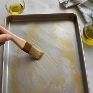 Olive oil being brushed over a rimmed baking sheet