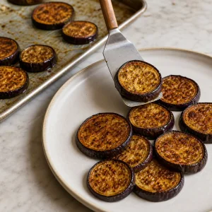 Roasted eggplant rounds being moved onto a serving platter