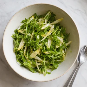 Frischer Rucola und geschnittener Endivie leicht mit Zitrus-Vinaigrette in einer Schüssel vermengt