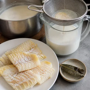Poached haddock on a plate beside smoky milk strained into a jug