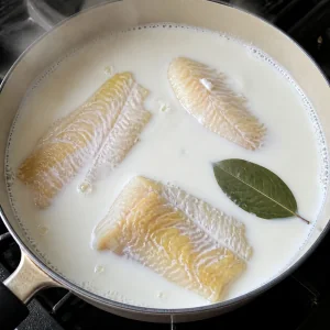 Smoked haddock fillets poaching in milk with a bay leaf