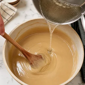 Hot sugar syrup poured slowly into tahini while stirring with a wooden spoon