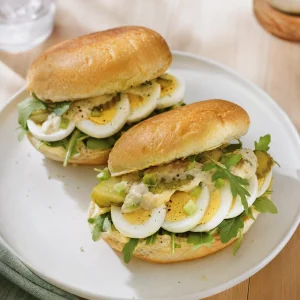 Finished sliced egg sandwiches with arugula and pickles on toasted rolls