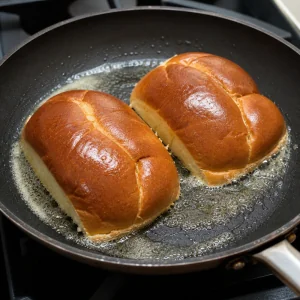Split rolls toasting in melted butter in a skillet