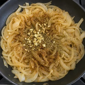 Garlic and spices scattered over softened onions in a skillet