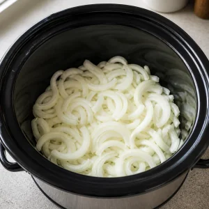 Sliced onions layered in the bottom of the slow cooker.