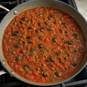 Puttanesca tomato sauce simmering with black olives, capers, and oregano.