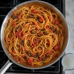 Spaghetti tossed in glossy puttanesca sauce with pasta water nearby.