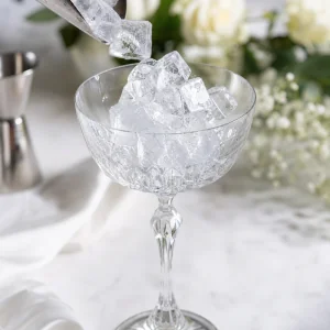 Taca coupe de cristal cheia de gelo para gelar antes de misturar o coquetel