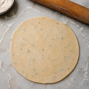 Sealed stuffed dough rolled gently into a thin round paratha.