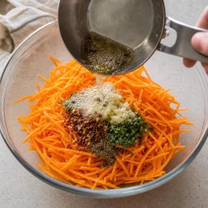 Hot oil being poured over garlic and spices on julienned carrots to bloom the aromatics.
