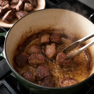 Cubetti di manzo infarinati che rosolano in olio caldo in una casseruola