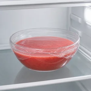A covered bowl of strawberry passion fruit mixture chilling on a refrigerator shelf.