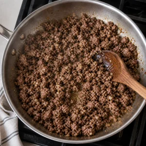 Ground lamb and minced garlic brown in a skillet while being broken up with a spoon.