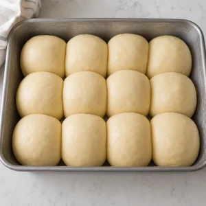 Dodici palline di impasto gonfie in una teglia unta per la seconda lievitazione
