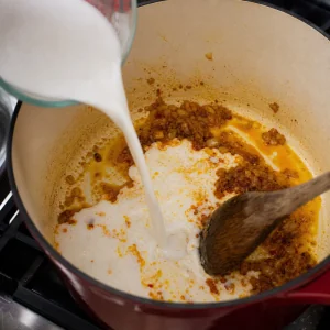 Coconut milk poured into red curry aromatics for the soup broth.
