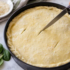 Fazer cortes de vapor na massa untada e polvilhar Parmigiano antes de assar