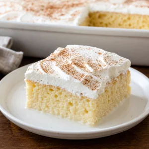 Slice of tres leches milk cake topped with whipped cream and cinnamon