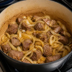 Cebollas en rodajas cocinándose con cordero dorado en una olla pesada