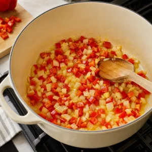 Diced onion and red bell pepper sauteing in olive oil in a large pot