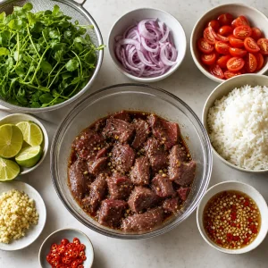 Marinated beef resting beside prepared watercress, tomatoes, onion, rice, and limes