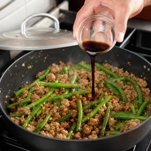 Sauce soja et vinaigre de riz verses sur la dinde et les haricots verts dans la poele