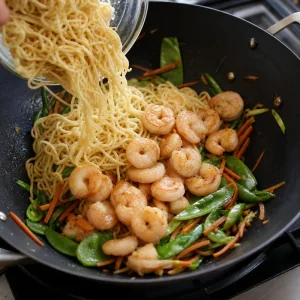 Nouilles cuites et crevettes saisies remises dans le wok avec les légumes.