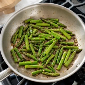 Asparagus pieces cooking in a skillet until bright green and tender-crisp.